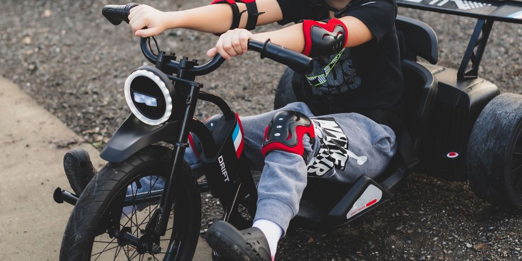 Child riding a small tricycle, wearing protective gear and smiling.
