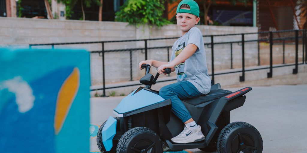 Child riding a blue toy vehicle in an outdoor setting.