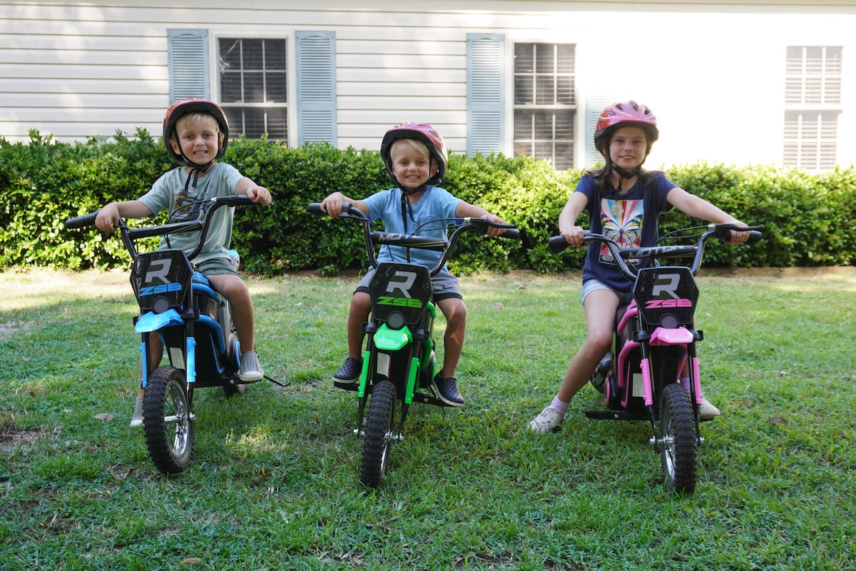 Kids riding colorful electric dirt bikes on a dirt trail.