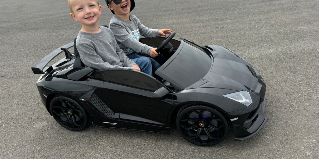 Two kids happily riding in a black toy sports car.