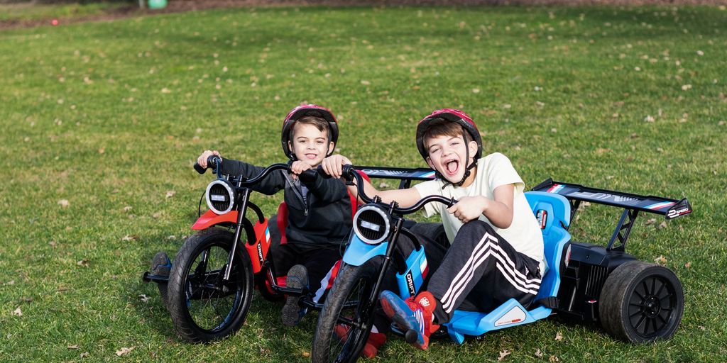 Two children riding small electric vehicles on green grass.