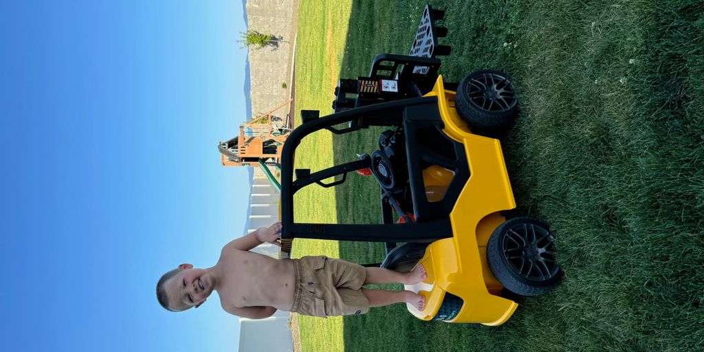 Child standing on a yellow ride-on vehicle in grass.
