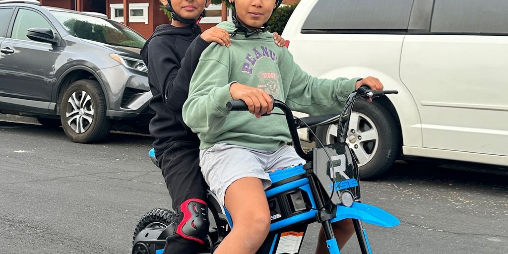 Two children riding a small blue electric bike together.