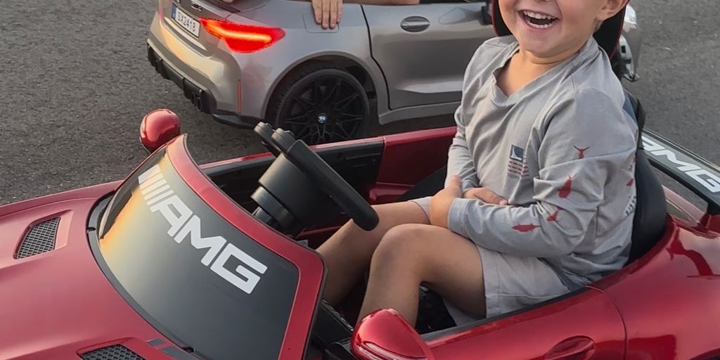 Two young children joyfully riding in toy sports cars.