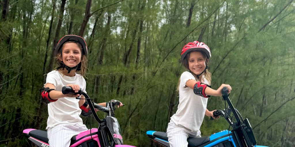 Two children riding electric bikes in a green outdoor setting.